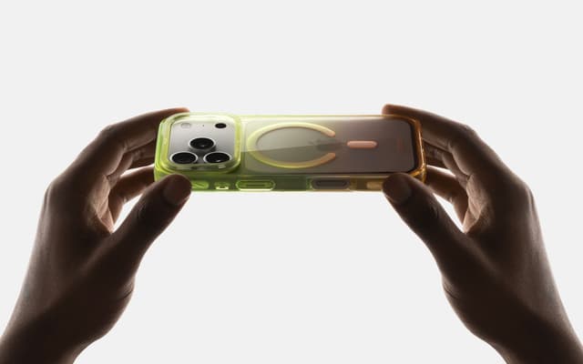Two hands gently flexing a green-tinted CLICK Clear Ombre case, its translucency and MagSafe ring showing against a plain backdrop