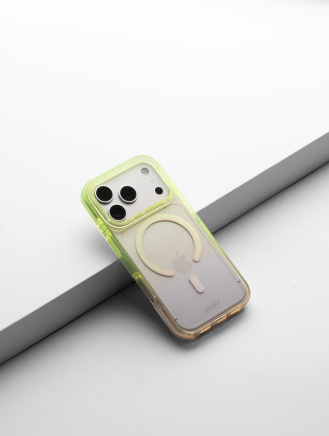 CLICK Clear Ombre MagSafe case with a neon-yellow top fading to a warm pink base, angled on a gray ledge