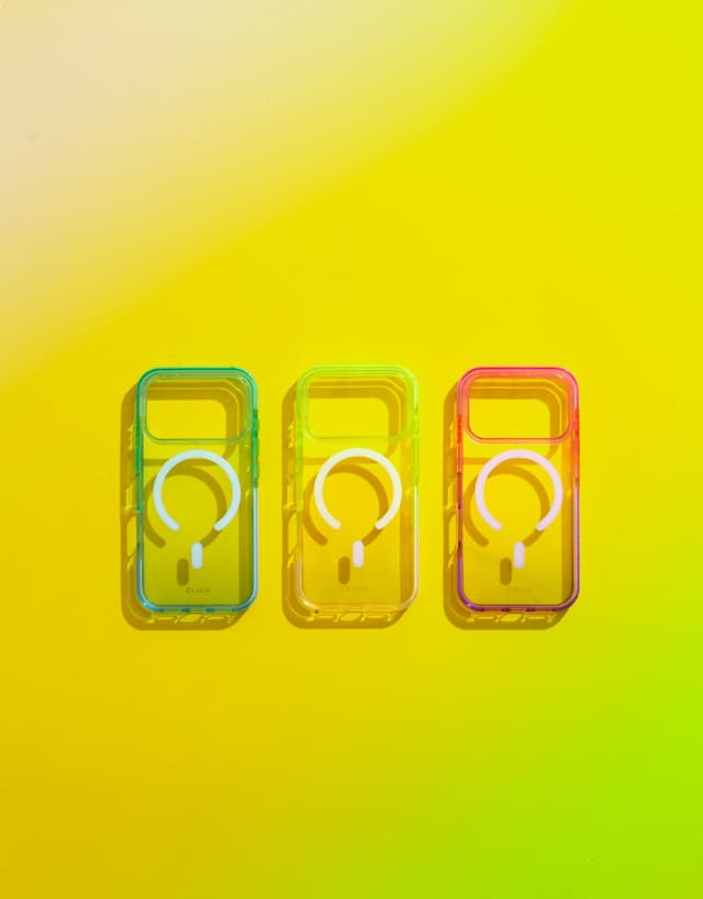 Three CLICK Clear Ombre cases with MagSafe rings laid diagonally across red, green, and yellow color-block panels