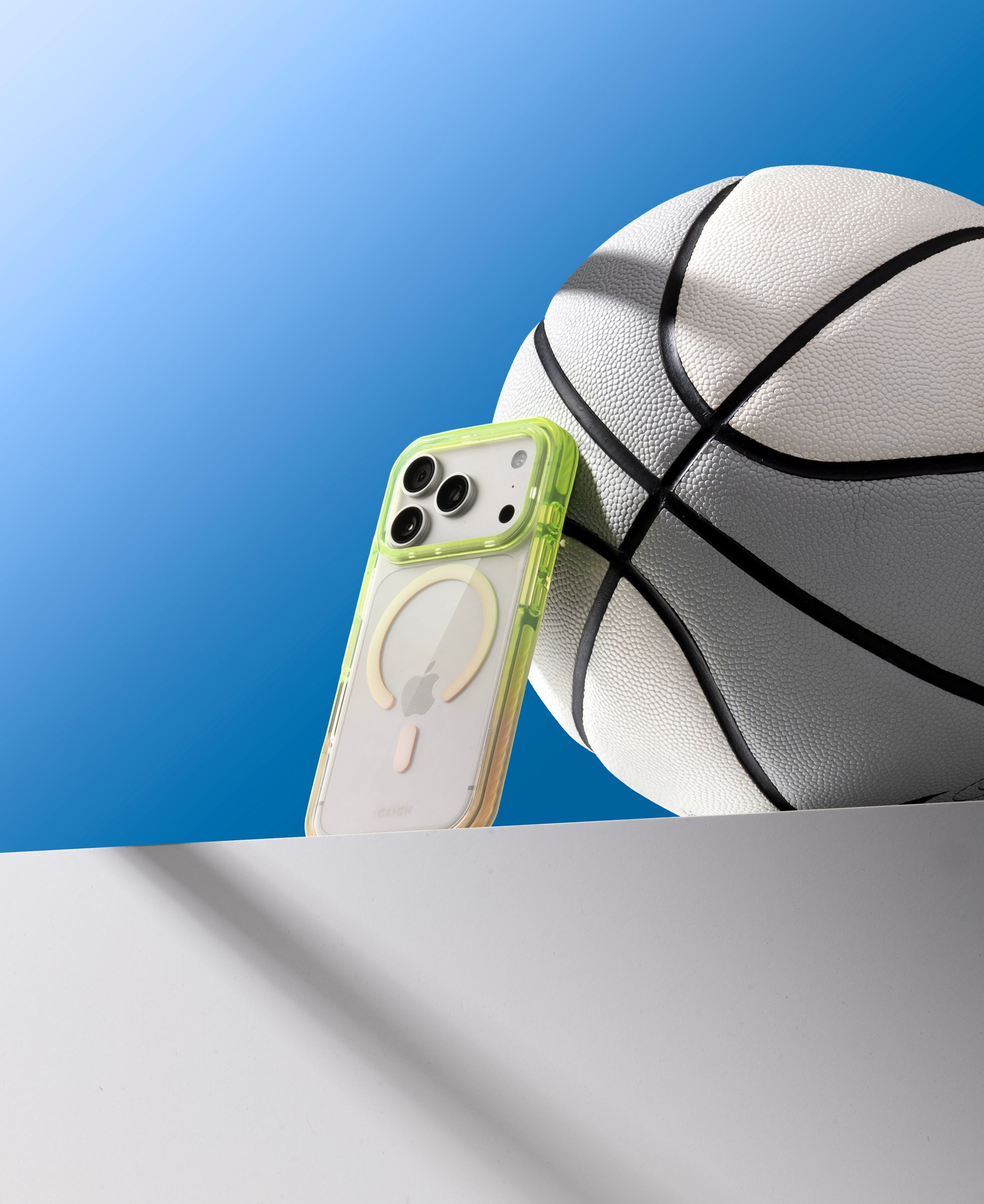 Green CLICK Clear Ombre case propped on a ledge against a basketball, blue gradient sky behind