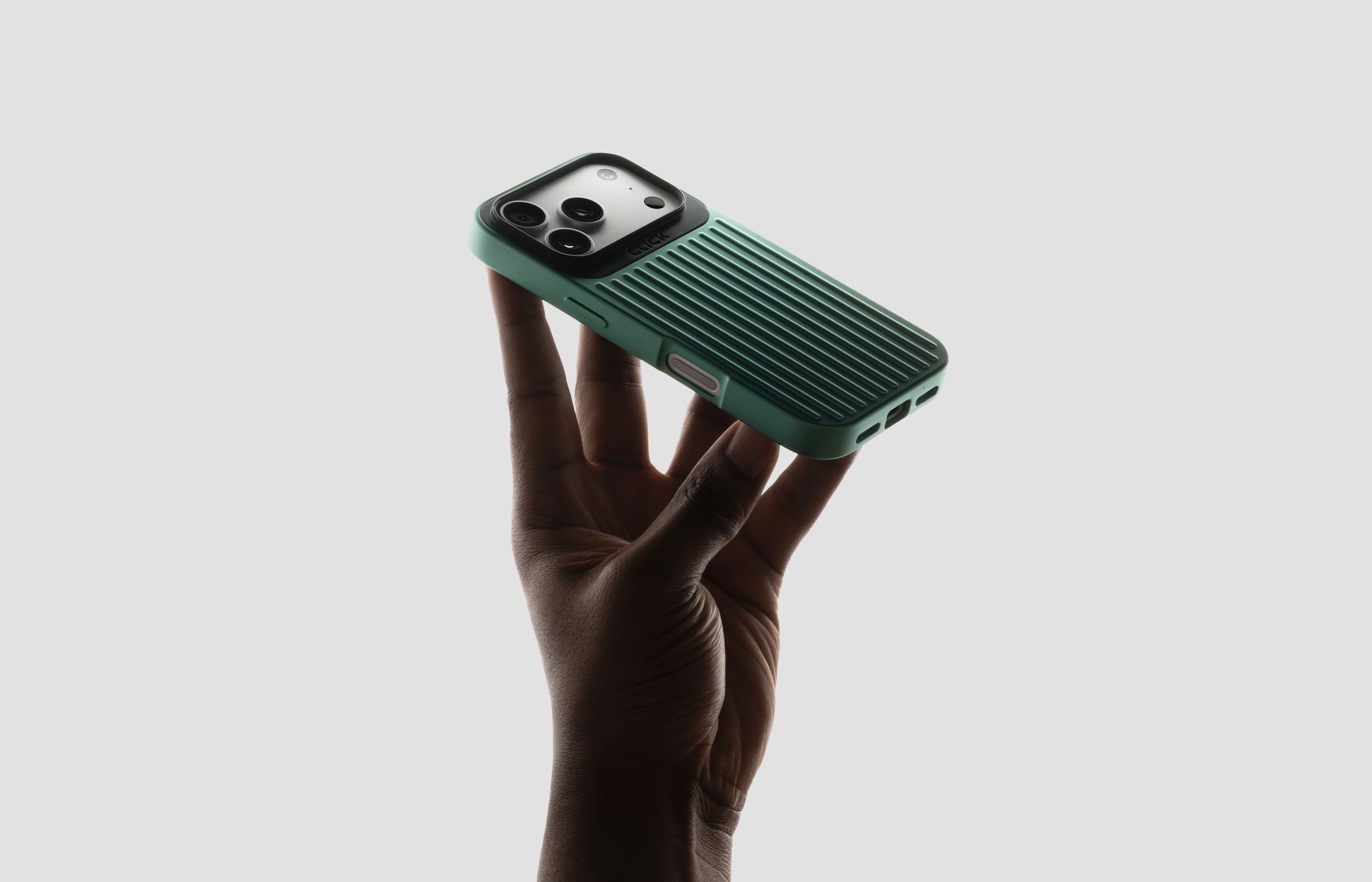 A sage green CLICK Nova case held in one hand against a pale wall