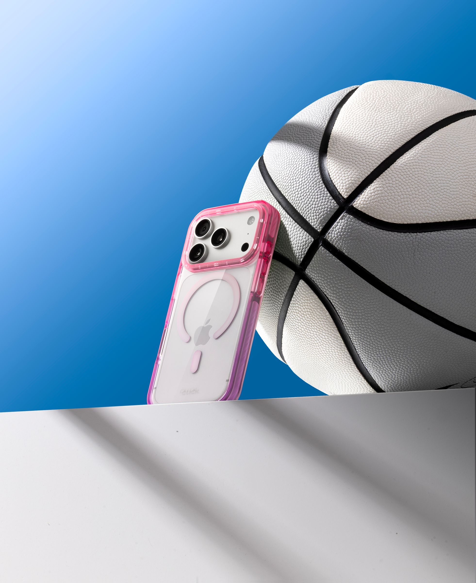 Pink CLICK Clear Ombre case propped against a basketball on a blue gradient background